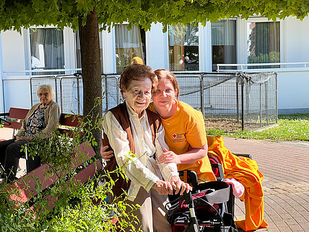 Pflegerin und Seniorin unter dem Baum sitzend