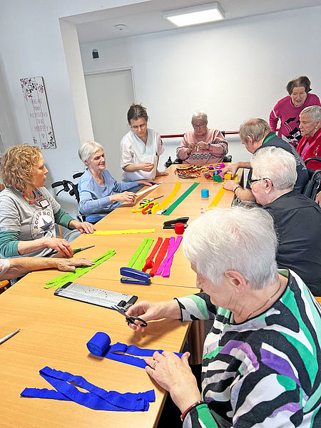 Seniorinnen und Senioren sitzen zusammen und basteln bunte Bänder