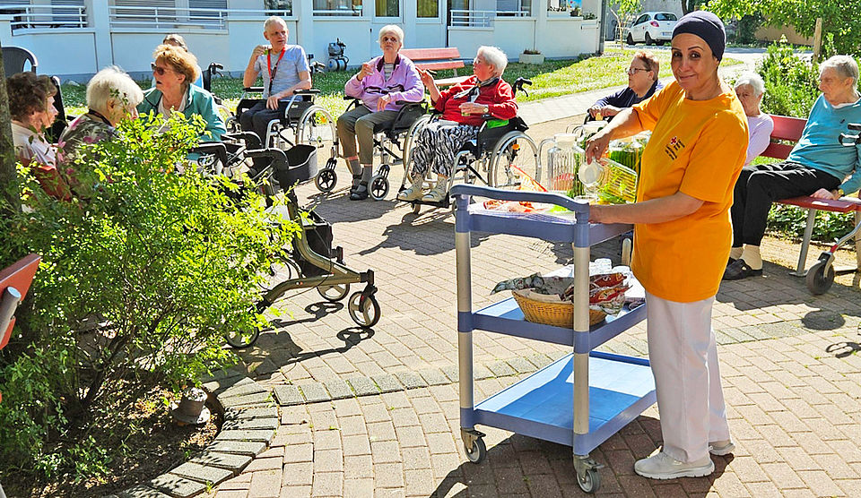 Senioren und eine Pflegerin genießen das schöne Wetter im Garten