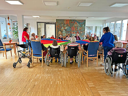 Im Herbst-Angebot arbeiten die SeniorInnen im Kreis sitzend mit einem farbenfrohen Schwungtuch