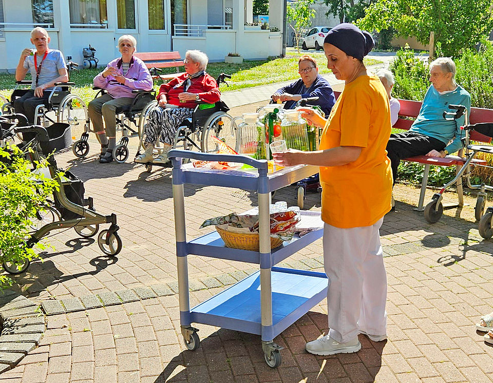 Eine Pflegerin schenkt den Senioren Maibowle ein