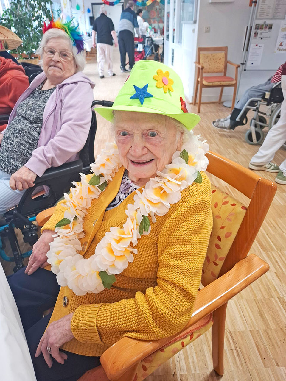 Mit Hut und Blumenkette verkleidete Senioren sitzt auf einem Stuhl